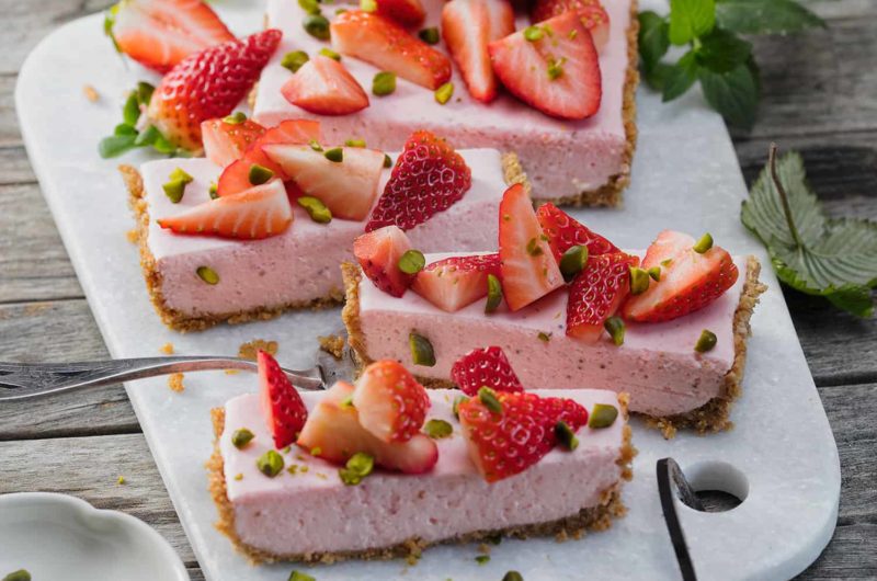 Erdbeerkuchen ohne Backen in Stücke geschnitten auf einem Brett.